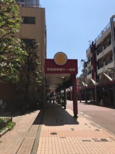 歩道沿いの商店街入口のアーチと周囲の街並みを写した写真。